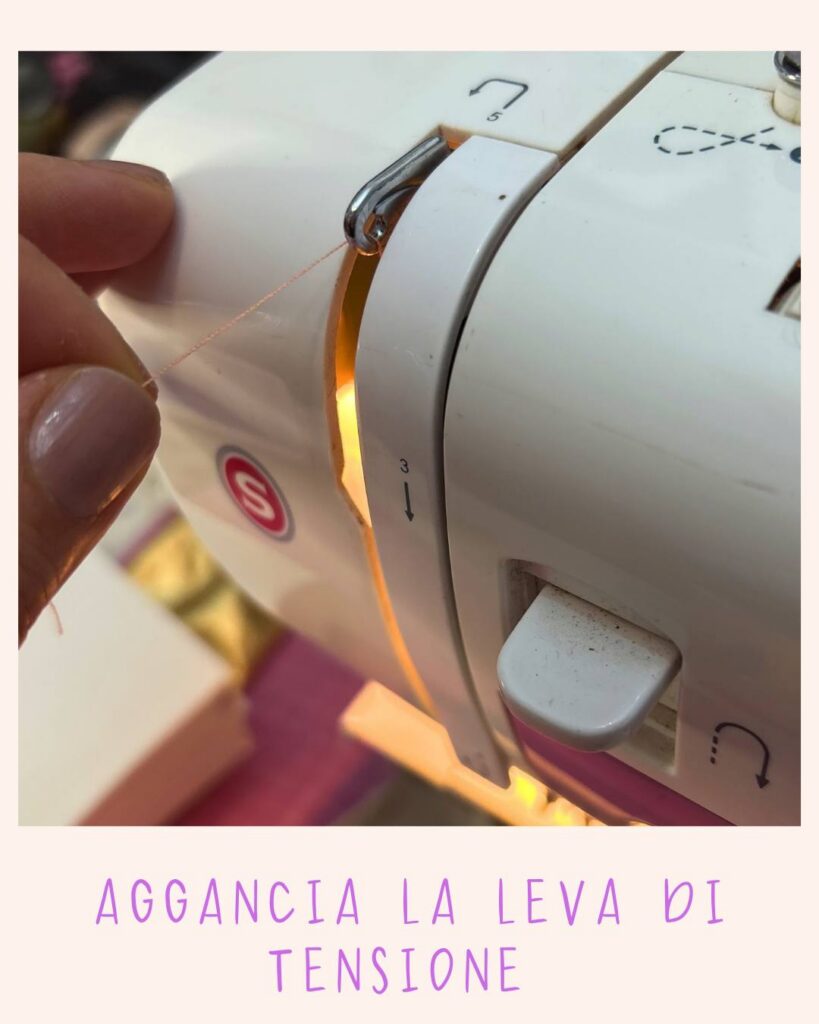 Mano che guida il filo agganciandolo alla leva di tensione laterale di una macchina da cucire Singer