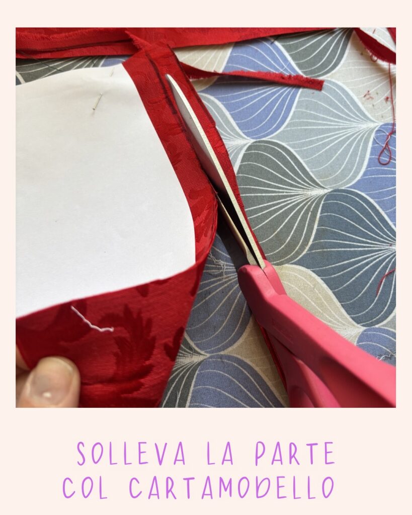 Forbici rosa che tagliano il tessuto rosso sollevando il cartamodello