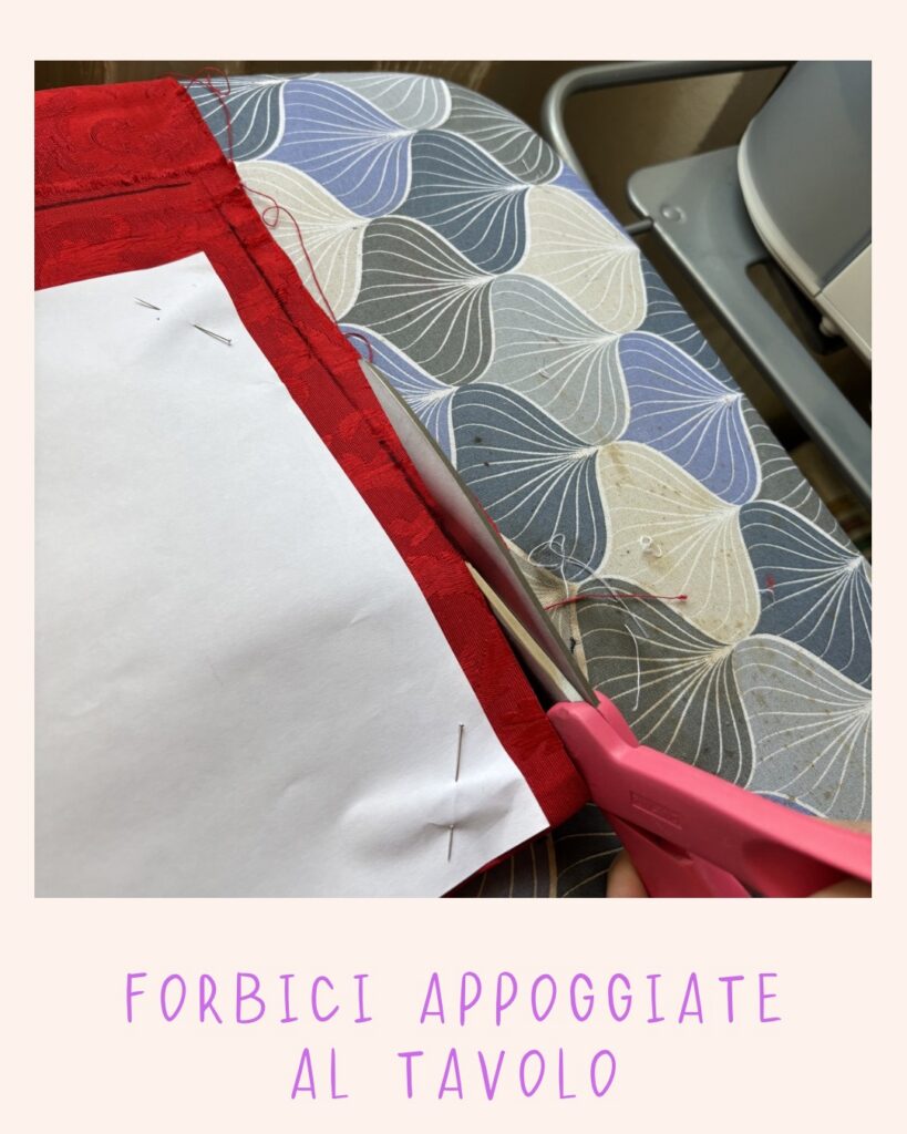 Forbici rosa appoggiate al tavolo mentre si taglia il tessuto rosso