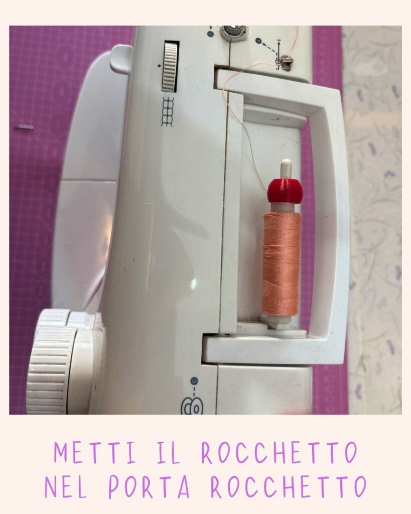 Rocchetto di filo arancione inserito nel porta rocchetto di una macchina da cucire bianca e rosa