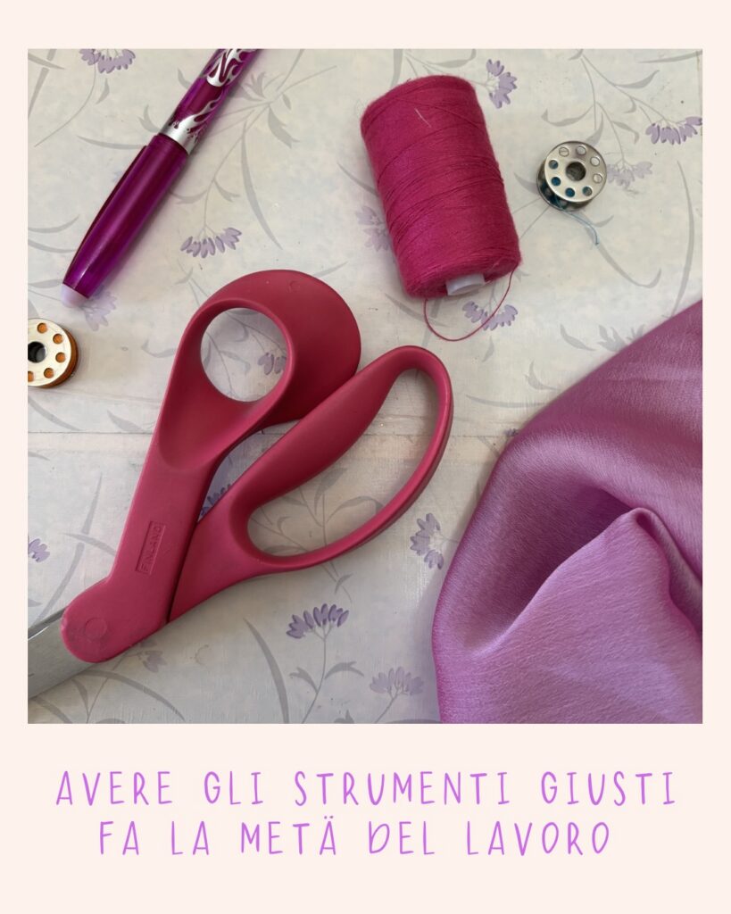 Forbici rosa appoggiate al tavolo insieme a filo rosa e tessuto rosa