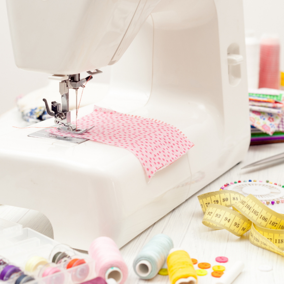 Macchina da cucire bianca con tessuto rosa, rocchetti colorati, metro e bottoni sul tavolo