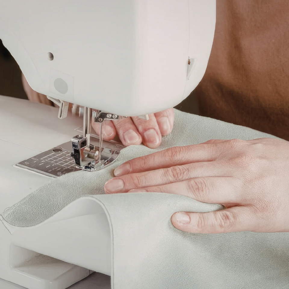 Mani sopra macchina da cucire che cuciono un tessuto azzurro